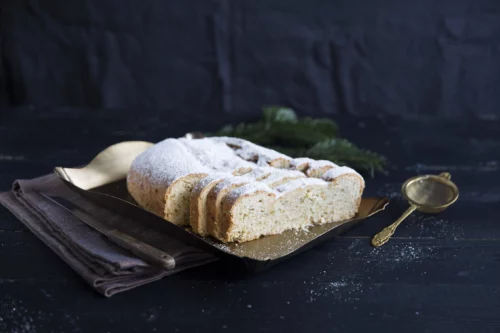 Aufgeschnittener Mandelstollen vor Tannenzweig und schwarzem Hintergrund