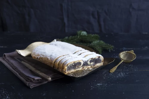 Aufgeschnittener Mohnstollen vor Tannenzweig und schwarzem Hintergrund