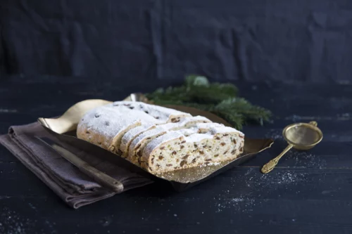 Aufgeschnittener Rosinenstollen vor Tannenzweig und schwarzem Hintergrund